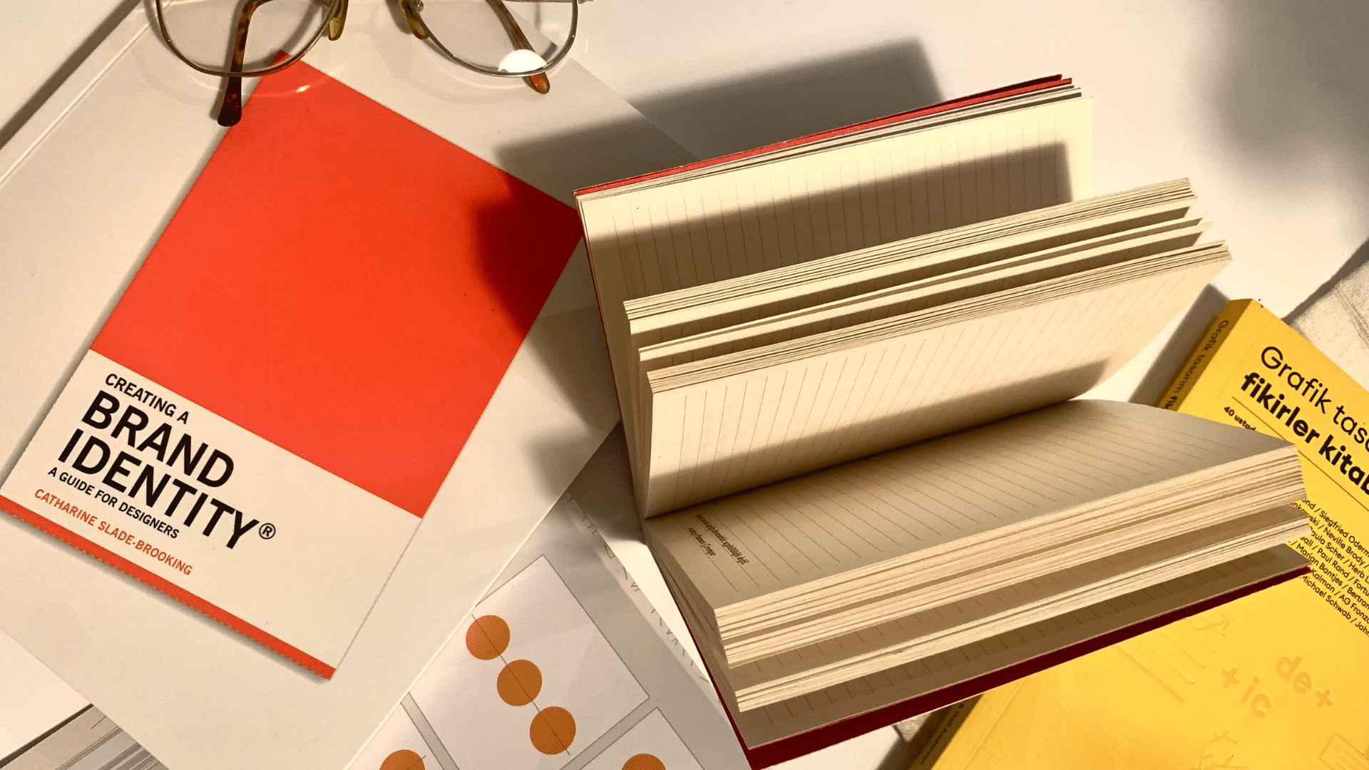 Libros de diseño gráfico sobre identidad de marca, reputación online, branding personal, tipografía y cuadernos abiertos sobre una mesa