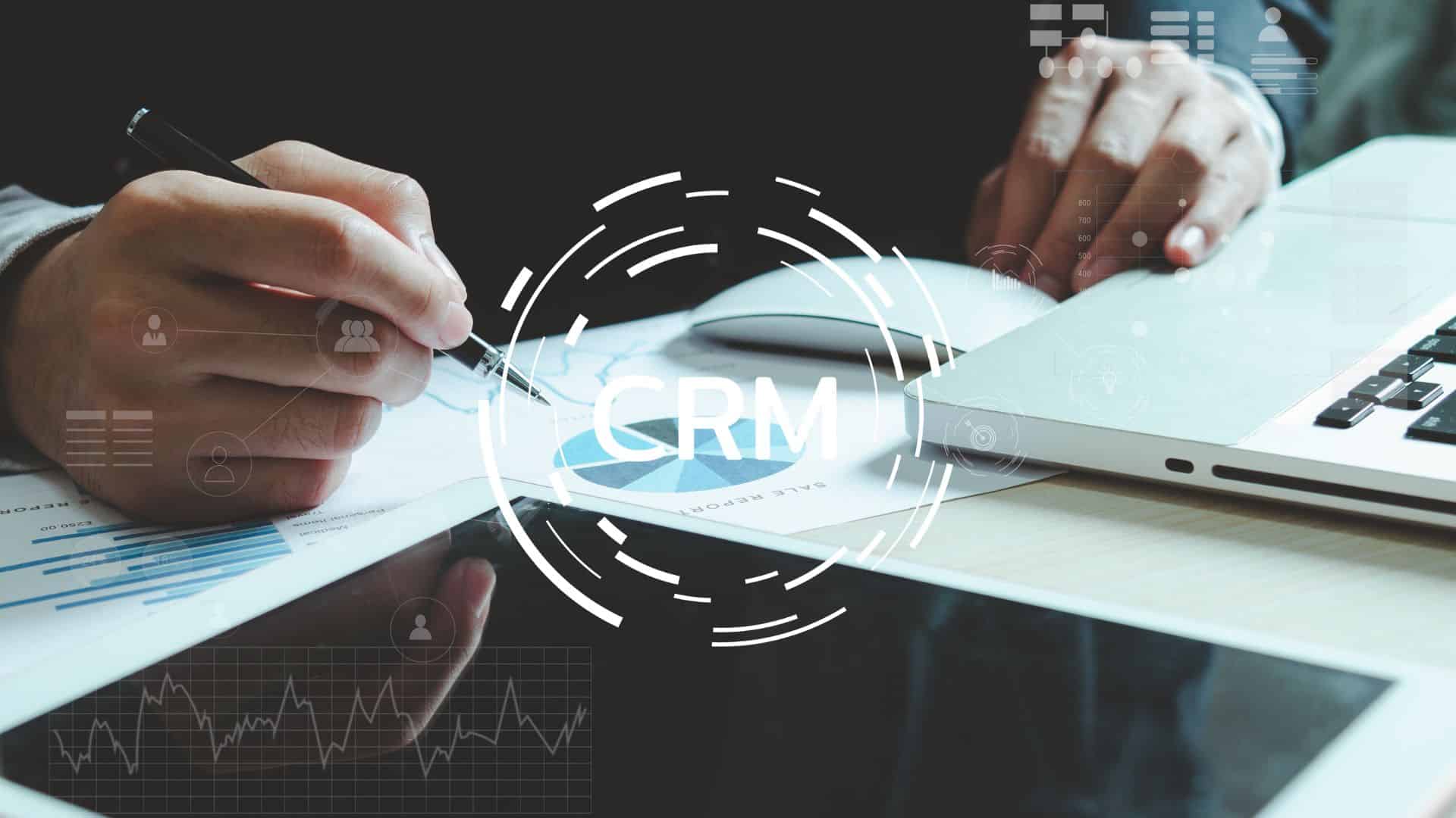 Manos trabajando con gráficos en papel y portátil, con icono de CRM y elementos digitales superpuestos de automatización de procesos