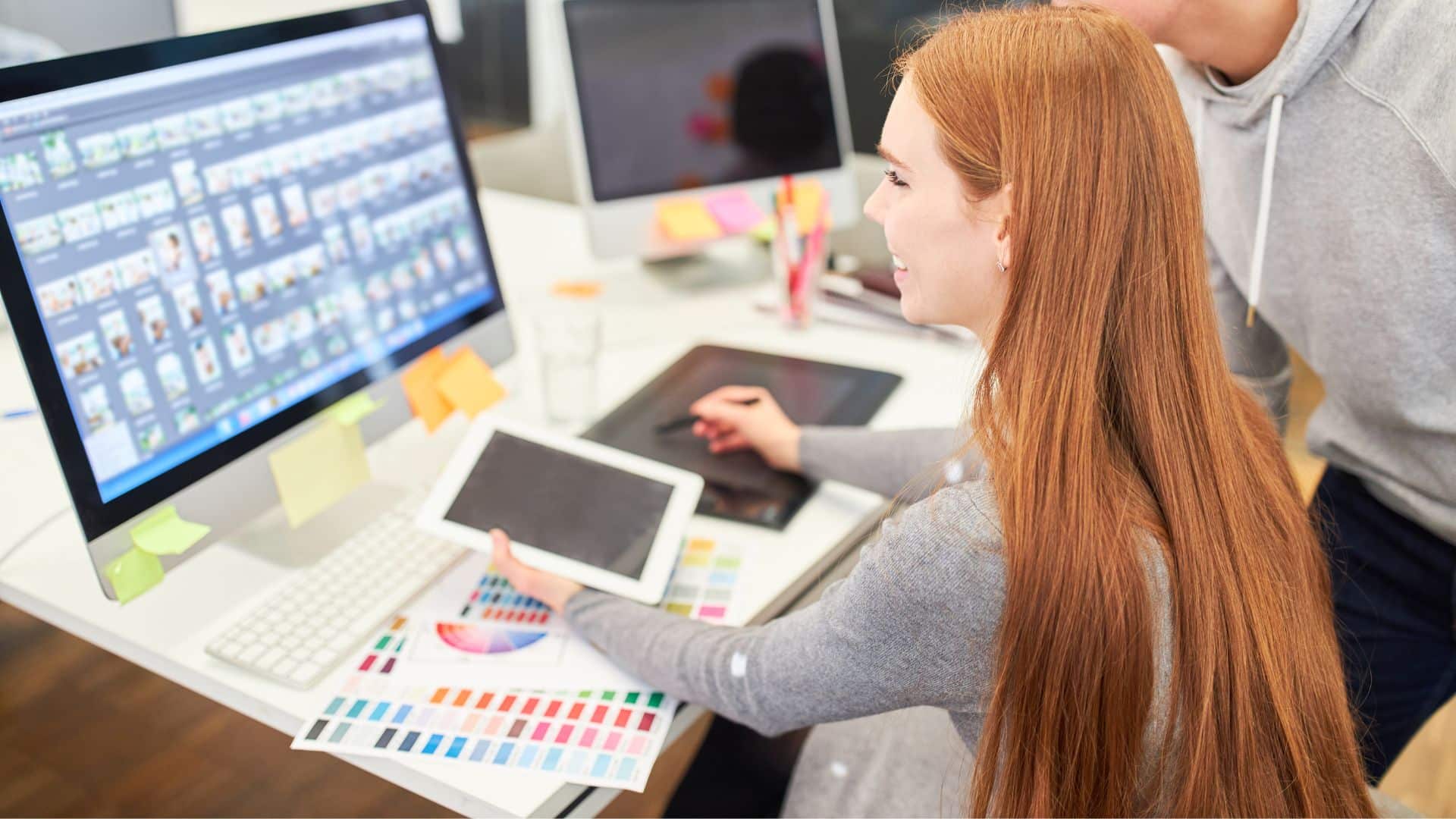 Diseñadora gráfica trabajando en una agencia de desarrollo con paletas de color y pantalla llena de miniaturas